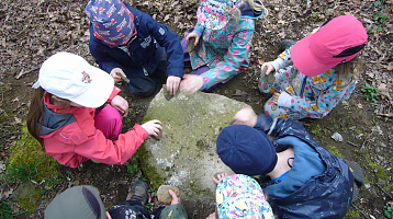 Kinder sitzen um einen großen Stein herum